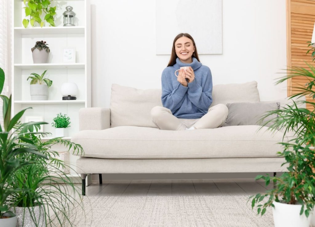 femeie zambitoare stand pe canapea intr-o camera cu plante de interior